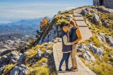 Couple man and woman tourists in mountain landscape at national park Lovcen, Montenegro. Travel to Montenegro concept clipart