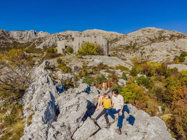 Kosmac Kalesi 'nin Çöken Kulesi' nin arka planında mutlu bir aile. Karadağ 'a seyahat. Antik Avusturya-Macaristan kalesi bir savunma yapısı ve gözlem noktası olarak inşa edildi. Montenego