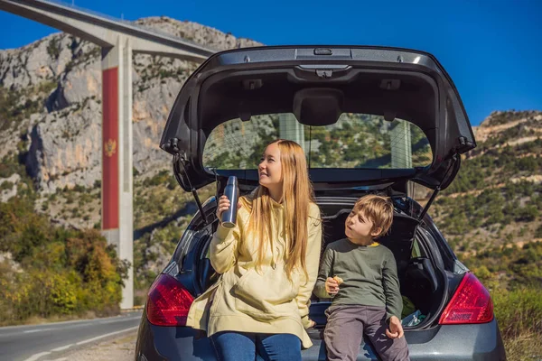 Montenegro. Mom and son tourists are sitting on the trunk of a car. Road trip around Montenegro. Bridge Moracica. Reinforced concrete bridge across the Moraci gorge. The motorway Bar - Bolyare. The — Foto Stock