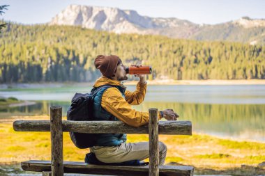 Kara Göl Crno Jezero 'nun panoramik sabah manzaralı arka planındaki erkek turist. Durmitor Nacionalni Park 'ın sakin yaz manzarası, Zabljak konumu, Karadağ, Avrupa. Doğa konseptinin güzelliği