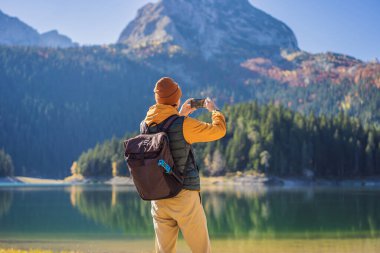 Kara Göl Crno Jezero 'nun panoramik sabah manzaralı arka planındaki erkek turist. Durmitor Nacionalni Park 'ın sakin yaz manzarası, Zabljak konumu, Karadağ, Avrupa. Doğa konseptinin güzelliği