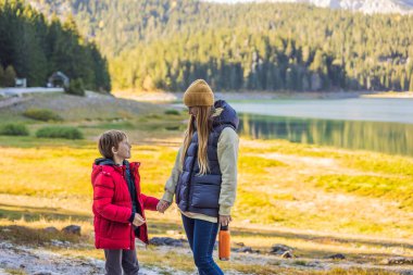 Anne ve oğul turistler Kara Göl Crno Jezero 'nun panoramik sabah manzarasının arka planında. Durmitor Nacionalni Park 'ın sakin yaz manzarası, Zabljak konumu, Karadağ, Avrupa. Doğanın güzelliği konsepti