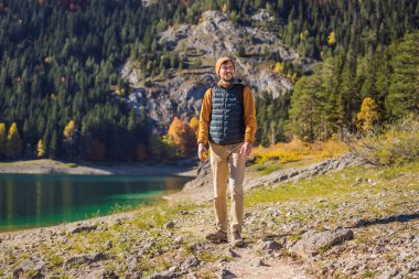 Kara Göl Crno Jezero 'nun panoramik sabah manzaralı arka planındaki erkek turist. Durmitor Nacionalni Park 'ın sakin yaz manzarası, Zabljak konumu, Karadağ, Avrupa. Doğa konseptinin güzelliği