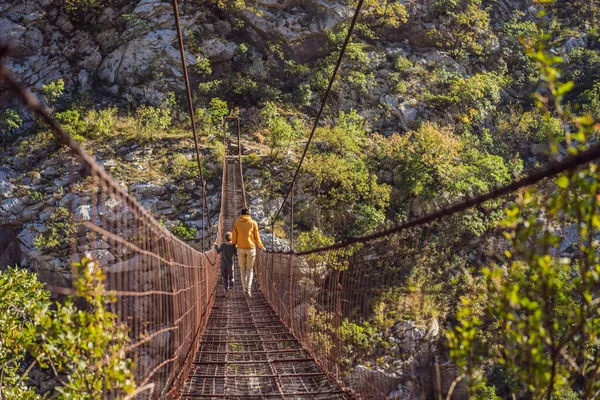 Father and son tourists on Old rusty bridge. Attraction Long extreme suspension iron bridge across the river Moraca. Sights of Montenegro. Landmark Montenegro — Stock Photo, Image