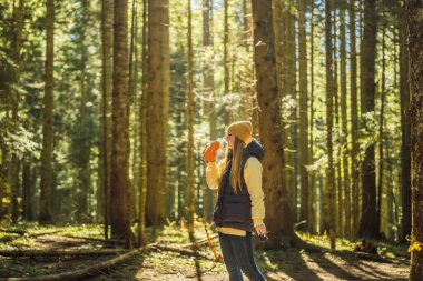 Sıcak giysiler içinde çay içen bir kadın çam ormanında yürümekten zevk alıyor.