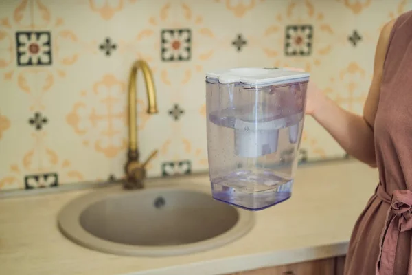Jug with water filter in hand in the kitchen.