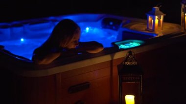 Gece sahnesi. Genç bir kadın çatıdaki jakuzide dinleniyor. Mumlara bakıyor..
