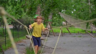 Sarı tişörtlü mutlu çocuk, okul çocuğu tırmanış parkında eğleniyor..