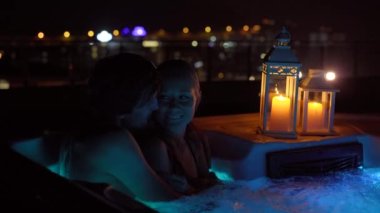 Genç bir adam ve bir kadın gecenin bir yarısı çatıdaki jakuzide dinleniyorlar. Mumlarla aydınlatılıyor..