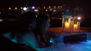 Genç bir adam ve bir kadın gecenin bir yarısı çatıdaki jakuzide dinleniyorlar. Mumlarla aydınlatılıyor..