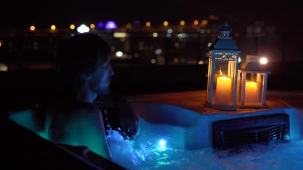 Young Man Relaxing Hot Tub Rooftop Night Lit Candles — Stockvideo