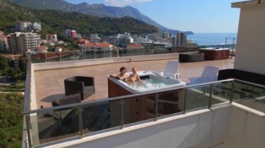 Yavaş çekim videosu. Bir erkek ve bir kadının çatıdaki jakuzide iyi vakit geçirip rahatlarken çekilmiş bir fotoğrafı..