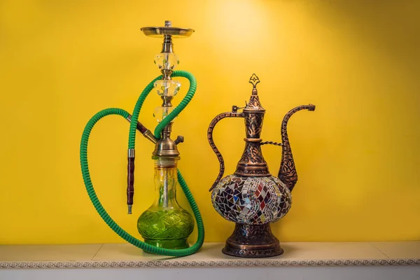 hookah shisha with glass flask and metal bowl with colored smoke on a yellow background. Traditional Eastern vacation for relaxation.