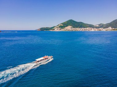 Turistlerle dolu feribot turkuaz suda yüzüyor. Drone görünümü.