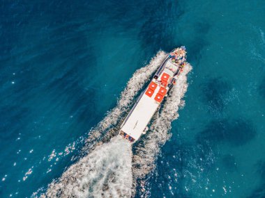 Turistlerle dolu feribot turkuaz suda yüzüyor. Drone görünümü.