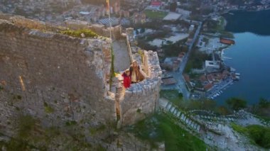 Hava videosu. Genç bir kadın ve küçük oğlu dağın tepesindeki Saint Johns Kalesi 'nin kulesinde duruyorlar. Kotor şehrinin muhteşem manzarasının tadını çıkarıyorlar.