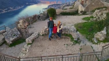 Hava videosu. Anne, baba ve oğuldan oluşan bir turist ailesi dağın tepesindeki Aziz John Kalesi 'nin kulesinde duruyorlar. Şehrin fantastik manzarasının tadını çıkarıyorlar.
