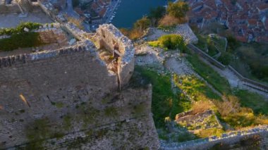 Yavaş çekim hava görüntüsü. Genç bir kadın turist dağın tepesindeki Saint Johns Kalesi 'nin kulesinde duruyor. Kotor şehrinin muhteşem manzarasının tadını çıkarıyor.