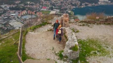 Hava videosu. Anne, baba ve oğuldan oluşan bir turist ailesi dağın tepesindeki Aziz John Kalesi 'nin kulesinde duruyorlar. Şehrin fantastik manzarasının tadını çıkarıyorlar.