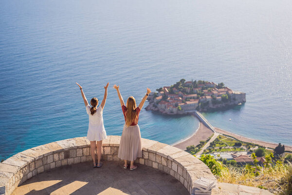 Two Woman tourist on background of beautiful view of the island of St. Stephen, Sveti Stefan on the Budva Riviera, Budva, Montenegro. Travel to Montenegro concept.