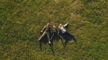 A family of three father, mother, and son are lying on the grass in a park. Drone moves upward.
