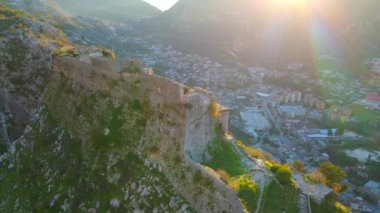 Yavaş çekim hava görüntüsü. Genç bir kadın turist dağın tepesindeki Saint Johns Kalesi 'nin kulesinde duruyor. Kotor şehrinin muhteşem manzarasının tadını çıkarıyor.