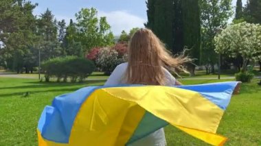 Young woman holding the Ukranian flag is running on a green loan. Refugees support. Restoration of Ukranian families.
