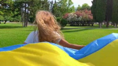 Ukrayna bayrağını tutan genç kadın yeşil bir krediyle koşuyor. Mültecilerin desteği. Ukraynalı ailelerin restorasyonu.