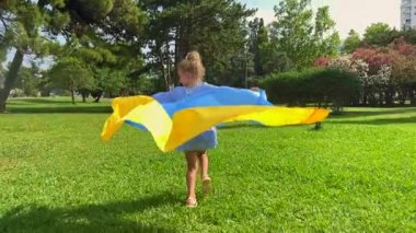 Slowmotion video. little girl holding the Ukranian flag is running on a green loan. Refugees support. Restoration of Ukraine.