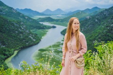 Skadar gölü kıyısındaki Rijeka Crnojevica Kanyonu 'nun arka planındaki kadın turist. Karadağ 'ın en ünlü manzaralarından biri. Nehir, dağlar arasında bir dönüş yapar ve geriye doğru akar..