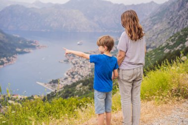 Anne ve oğul gezginler Kotor 'un manzarasından hoşlanırlar. Karadağ. Kotor Körfezi, Kotor Körfezi, Boka Kotorska ve eski şehrin duvarları. Karadağ 'a seyahat. Kotor 'un tahkimatları UNESCO Dünyasında
