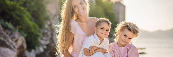 BANNER, LONG FORMAT Mother and two children daughter and son tourists on background of beautiful view St. Stephen island, Sveti Stefan on the Budva Riviera, Budva, Montenegro. Travel to Montenegro