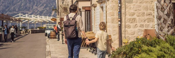BANNER, LONG FORMAT Dad and son tourists enjoying Colorful street in Old town of Perast on a sunny day, Montenegro. Travel to Montenegro concept. Scenic panorama view of the historic town of Perast at