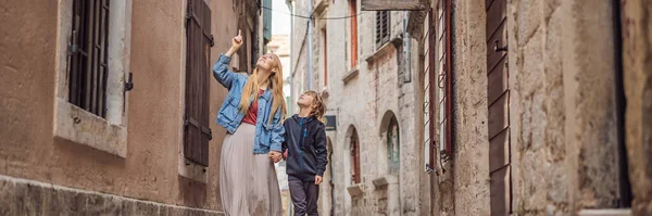 BANNER, LONG FORMAT Mom and son travelers enjoying Colorful street in Old town of Kotor on a sunny day, Montenegro. Travel to Montenegro concept.