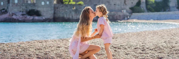 BANNER, LONG FORMAT Mother and daughter tourists on background of beautiful view St. Stephen island, Sveti Stefan on the Budva Riviera, Budva, Montenegro. Travel to Montenegro concept.