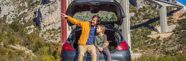 BANNER, LONG FORMAT Montenegro. Dad and son tourists are sitting on the trunk of a car. Road trip around Montenegro. Bridge Moracica. Reinforced concrete bridge across the Moraci gorge. The motorway