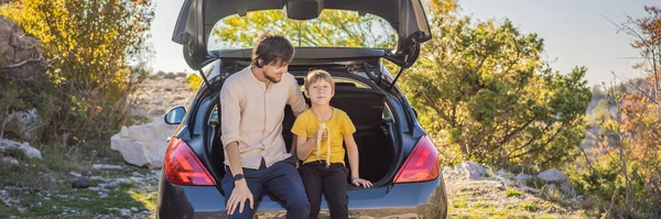 Dad and son are resting on the side of the road on a road trip. Road trip with children concept. BANNER, LONG FORMAT