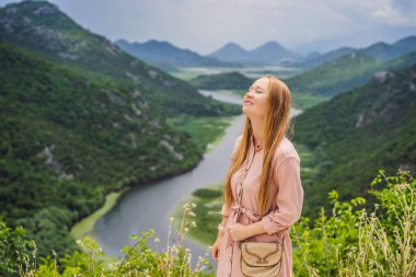 Skadar gölü kıyısındaki Rijeka Crnojevica Kanyonu 'nun arka planındaki kadın turist. Karadağ 'ın en ünlü manzaralarından biri. Nehir, dağlar arasında bir dönüş yapar ve geriye doğru akar..