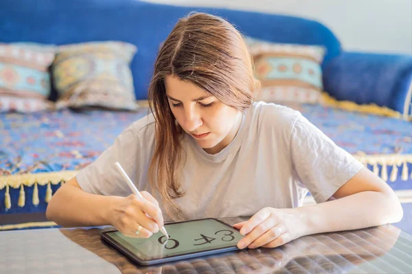 Calligrapher Young Woman writes phrase on digital tablet. Inscribing ornamental decorated letters. Calligraphy, graphic design, lettering, handwriting, creation.