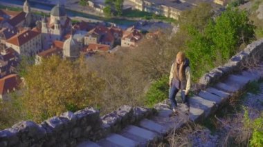 A young woman tourist visits the old town of Kotor in Montenegro. She is enjoying fabulous view of the city climbing up the stairs to the st.Johns fortress over the city. Travel to Montenegro concept