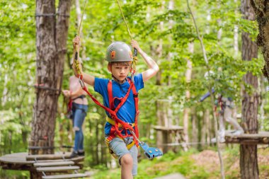 Anne ve oğlu ağaçtaki karabina emniyet halatıyla ağaçtan ağaç tepesindeki macera parkına giden aşırı yol tramvayına tırmanıyorlar. Aile hafta sonu çocuk aktiviteleri konsepti.