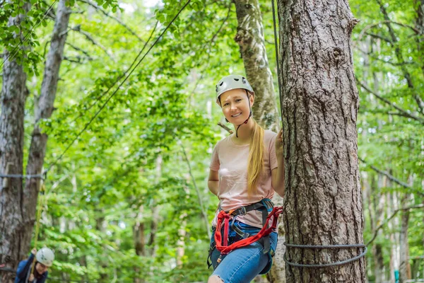Happy women girl female gliding climbing in extreme road trolley zipline in forest on carabiner safety link on tree to tree top rope adventure park. Family weekend children kids activities concept.