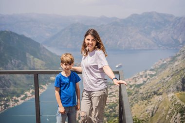 Anne ve oğul gezginler Kotor 'un manzarasından hoşlanırlar. Karadağ. Kotor Körfezi, Kotor Körfezi, Boka Kotorska ve eski şehrin duvarları. Karadağ 'a seyahat. Kotor 'un tahkimatları UNESCO Dünyasında