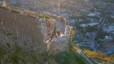Yavaş çekim hava görüntüsü. Genç bir kadın turist dağın tepesindeki Saint Johns Kalesi 'nin kulesinde duruyor. Kotor şehrinin muhteşem manzarasının tadını çıkarıyor.