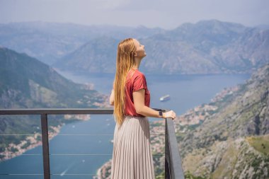 Kadın turist Kotor 'un manzarasından hoşlanıyor. Karadağ. Kotor Körfezi, Kotor Körfezi, Boka Kotorska ve eski şehrin duvarları. Karadağ 'a seyahat. Kotor 'un tahkimatları UNESCO Dünya Mirası' nda.