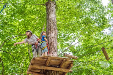 Anne ve oğlu ağaçtaki karabina emniyet halatıyla ağaçtan ağaç tepesindeki macera parkına giden aşırı yol tramvayına tırmanıyorlar. Aile hafta sonu çocuk aktiviteleri konsepti.