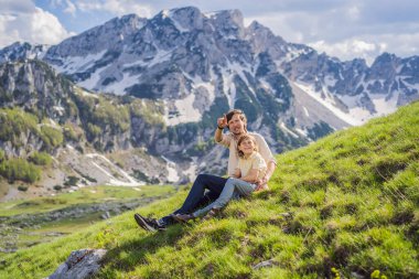 Karadağ 'ın Durmitor Dağı' ndaki Dağ Gölü manzarasında baba ve oğul turist ailesi güzel Durmitor Ulusal Parkı 'nda göl buzulu ve dağları yansıtıyor..