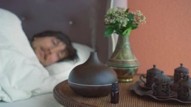 Genç bir adam yatağında uyuyarak koku yayıcısının yarattığı atmosferin tadını çıkarıyor. Sonra iyice dinlenmiş olarak uyanır. Aromaterapi Konsepti. Elektrik Ultrasonik Temel Yağ Aroma Yayıcı ve Nemlendirici