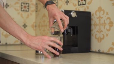 Mutfakta kahve makinesi kullanan genç bir adam var. Çerçevelemeyi kapat