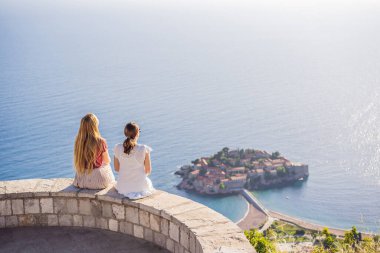 Two Woman tourist on background of beautiful view of the island of St. Stephen, Sveti Stefan on the Budva Riviera, Budva, Montenegro. Travel to Montenegro concept.